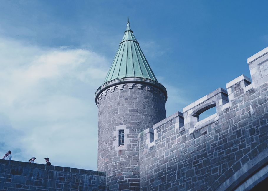 Low angle view of a historic castle tower and walls under a blue sky.