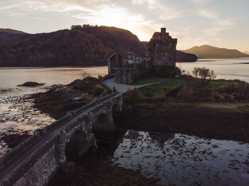 A captivating view of Eilean Donan Castle against a serene Scottish landscape at sunset.